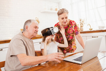 granddaughter with grandparents playing on a laptop and wearing virtual reality glasses