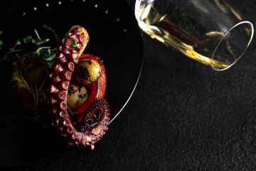 Sea delicacy grilled octopus with grilled vegetables. Dishes on a dark decorated background with a glass of wine