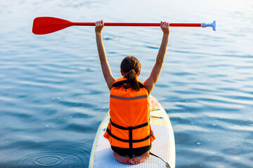young woman in orange life jacket on supboard at river