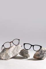 Two pairs of trendy glasses in plastic frame on stones on light background. Glasses sale poster....
