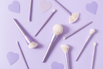 Fototapeta na wymiar Different make up brushes, favourite make up tools on violet background with hearts. Professional make up brushes for visagist. Cosmetic composition. Magazine, cosmetics store background