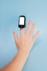 A hand with a heart rate monitor on a finger on a blue background with a place for text and a cut-out place on the gadget: measurement of heart rate and oxygen, vertical image