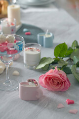 Peony pink rose with wax hearts, heart-shaped candle on the background of other candles on the table.