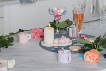Wax hearts on the table against the background of candles, flowers, champagne glasses.
