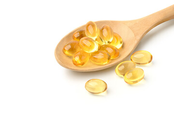 Golden color oil in soft gel capsules with wooden spoon isolated on white background.