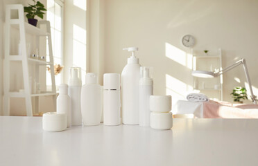 Obraz na płótnie Canvas Set of different white clean bottles with natural cosmetics standing on table of beauty salon. Close up of mock up bottles and containers of body care cosmetics on bright interior background.