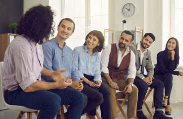 Group of happy interested business people listening to a coworker sitting in the office during a meeting. Creative young man talking to team members and telling a story about professional motivation