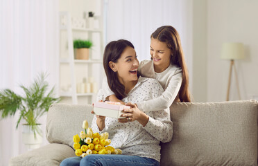 Caring small teen girl child make surprise to excited young mom congratulate with mothers day....