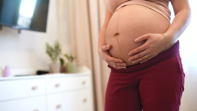 A pregnant woman gently stroking her big belly at home. The concept of waiting for a child, pregnancy and Maternity prenatal care
