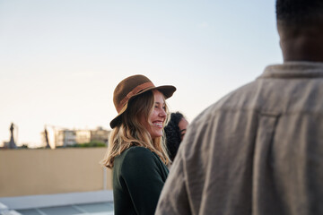 Caucasian female smiling, talking to diverse group of friends standing together on rooftop at party in the city
