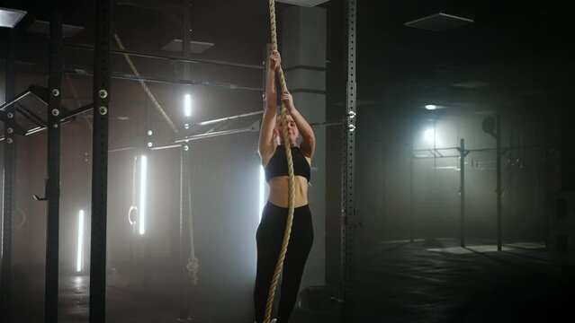 sporty exercise for endurance and power, woman is climbing rope in fitness hall