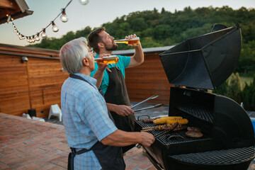 Pensioner spending time with son while drinking beer and barbecuing in the backyard
