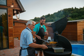 Young adult man preparing barbecue with his dad in the backyard near the pool