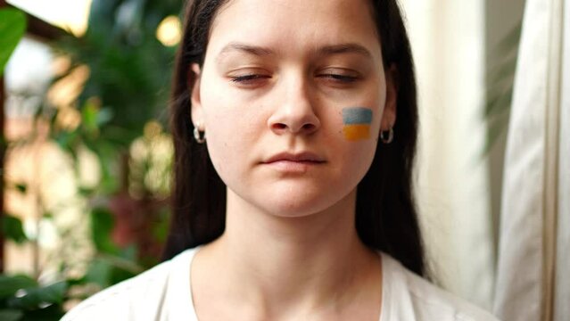 A sad young Ukrainian girl with the flag of Ukraine on her face is looking to camera. The concept of participation of the Ukrainian people in the war with Russia. Not war concept
