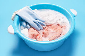 Basin of towels in soapy foam and rubber gloves on blue background close-up.