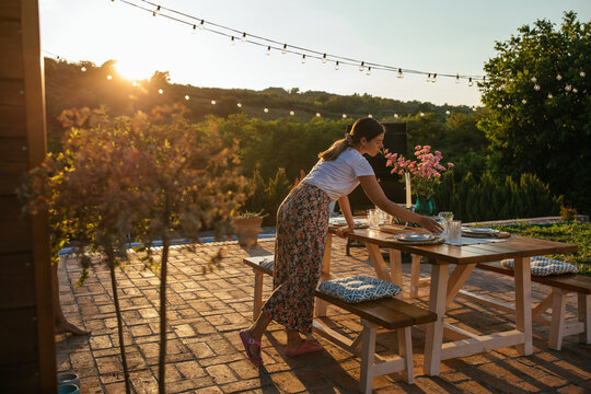 Young woman prepares table for friends and family dinner in the backyard