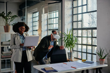 African businesswoman using laptop while her colleague using vr in office