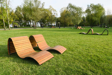 The concept of recreation in a city park. Sun loungers and benches on the lawn with a neatly trimmed lawn without people. Panorama of a well-groomed lawn with beautiful stripes after mowing.