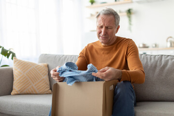 Sad mature man unpacking wrong parcel, delivery mistake