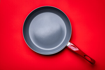 Top view of an empty grey ceramic pan with the red handle on the red background