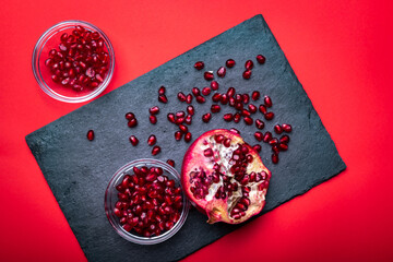Detail of the fresh pomegranate seeds and juicy pomegranate fruit on the dark slate plate on the red background.