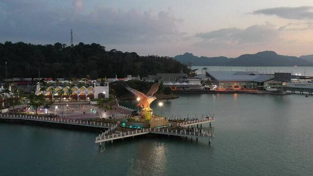 Cinematic drone fly around famous tourist attraction, dataran lang, illuminated eagle square in kuah town at dusk, langkawi island, kedah, archipelago of malaysia.