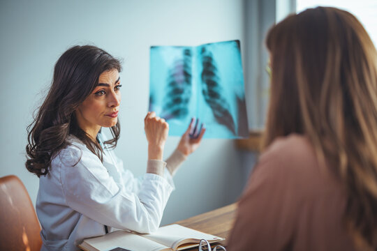 Female doctor explaining checkup result to her patient using x-ray image. Medicine professional showing diagnosis of x-ray image to patient sitting at clinic.