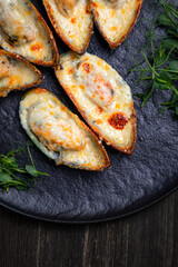 Fototapeta na wymiar baked mussels with cheese, on a dark plate with herbs and lemon on a wooden background