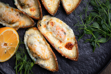 baked mussels with cheese, on a dark plate with herbs and lemon on a wooden background