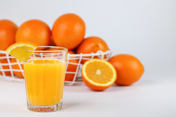 A glass of fresh orange juice and a basket with fresh oranges

