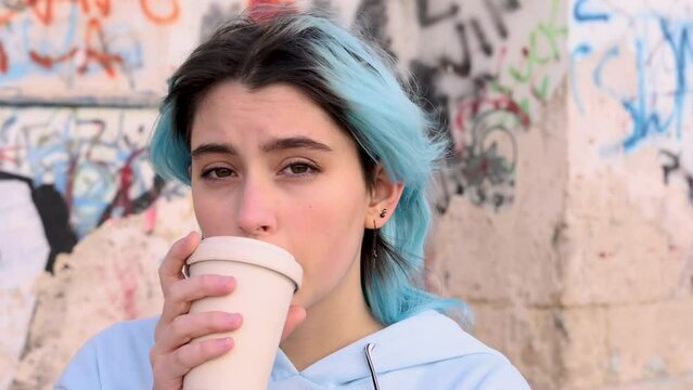 Teenage girl in blue oversize hoodie drinking coffee to go. Blue haired teen girl staying outdoors near graffiti wall. Mockup, head shot. Hipster and adolescence concept