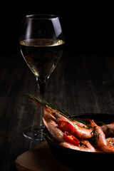 spicy langoustines with pepper and rosemary in a frying pan, served with a glass of wine
