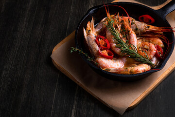 spicy langoustines with pepper and rosemary in a frying pan, served with a glass of wine