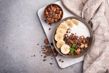 Healthy breakfast of granola with fresh banana, nuts, chocolate drops and yogurt