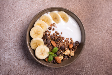Healthy breakfast of granola with fresh banana, nuts, chocolate drops and yogurt