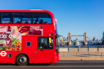 Red London bus crossing London Bridge, with Tower Bridge in background.