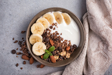 Healthy breakfast of granola with fresh banana, nuts, chocolate drops and yogurt