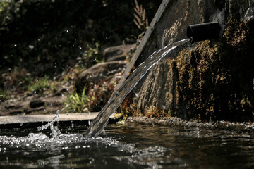 Pipe from a fountain releasing water onto a large stone container for cattle to drink in a village and releasing small droplets of water splashing around