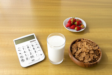 電卓と朝食（フレーク、苺、牛乳）。食費のイメージ