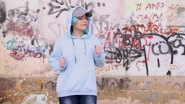 Teenager in light blue oversize hoodie and jeans Smiling and dancing. Blue haired teen girl outdoor against graffiti wall. Clothing mockup