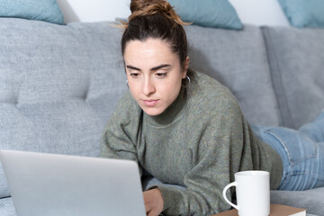 Young copywritter working on laptop while lying on sofa.