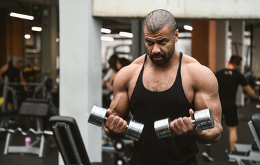 Fototapeta na wymiar Muscular afro-american man working out in gym doing exercises with dumbbells at shoulders without coach or instructor. Fitness crossfit bodybuilding concept