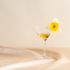 Cocktail glass with a flower, set on pink wavy satin in front of a pink background. Spring and summer minimal abstract concept. Isometric layout. Square with copy space