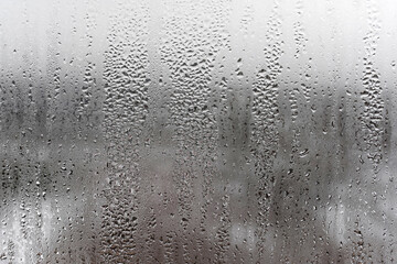 Naklejka premium Steamy window with water drops made in dull day, condensation on glass with drops flowing down, humidity and foggy blank