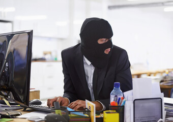 Doing some illegal activities.... Shot of a hacker dressed in a black mask hacking a computer.