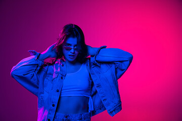Youth culture. Beautiful young emotional girl, student with long dark hair isolated on gradient pink-blue background in neon light.