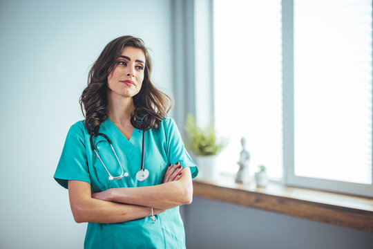 Female nurse wearing green scrubs, arms crossed. Medical professional working in hospital. Attractive female doctor at work. Smiling  female nurse in medical scrubs