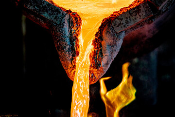 Molten metal flows out of the bucket. Soft focus