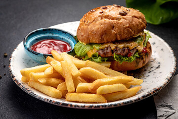 burger with fried steak vegetables and cheese, served with french fries and sauce, on a dark background