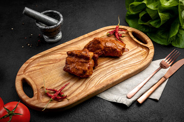 spicy ribs served on a board with hot chili peppers, on a dark background